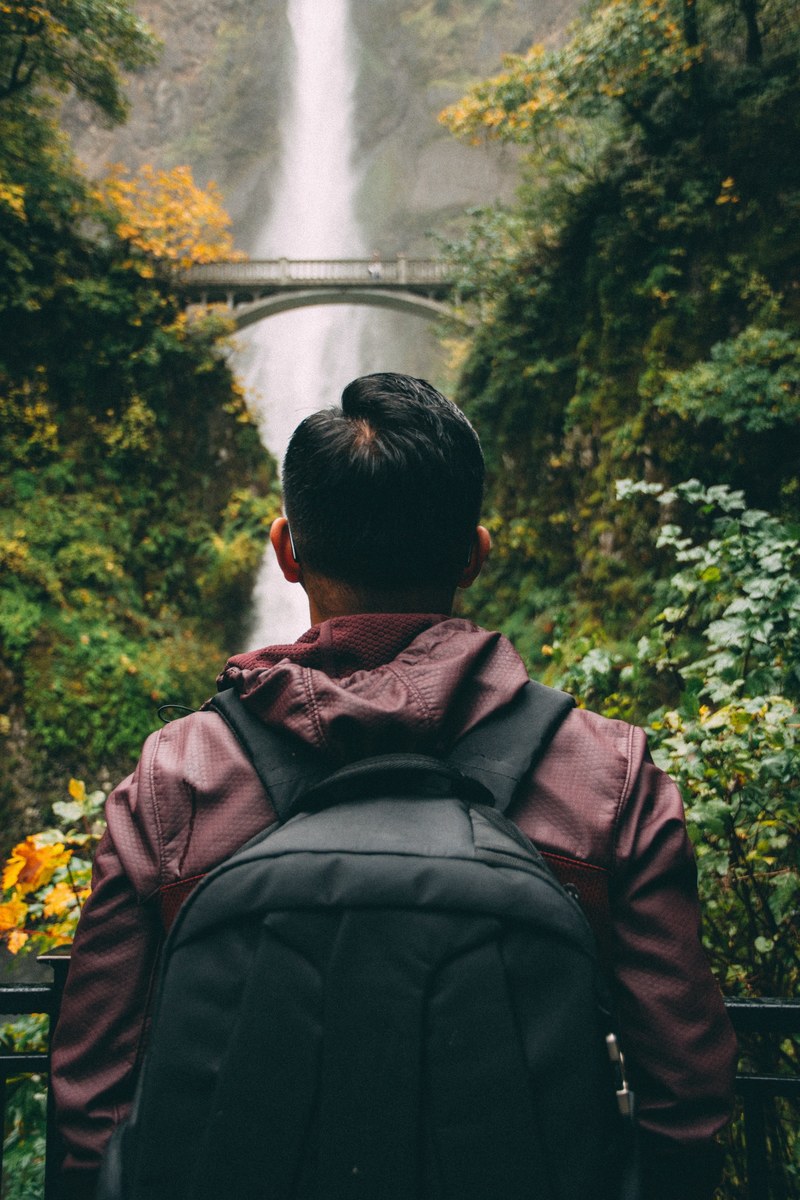 backpacker hikes alone towards a waterfall behind a bridge, multnomah falls 4k
