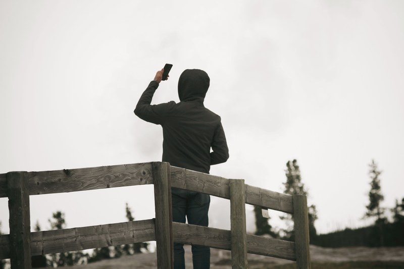 a man in a hoodie faces away by a wooden fence taking a selfie, man taking a selfie 4k