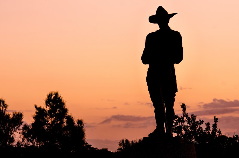 silhouette of person with scarecrow style hat looking out towards sunset, silhouette of person looking towards sunset 4k
