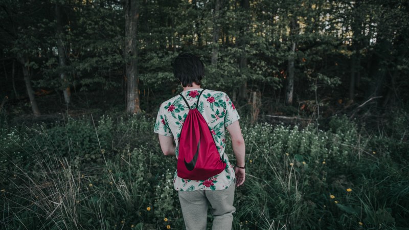 a person with a red back on their back standing back to camera in a forest, lost 4k