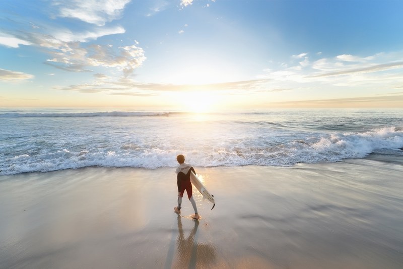 surfer with a surfboard walking towards the ocean on the sand beach in san diego at sunset, surf town 4k