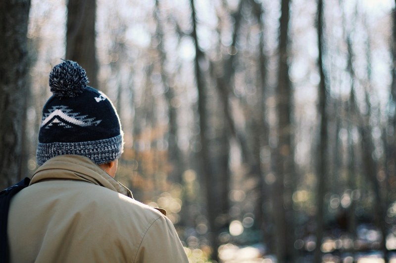 a man in a knit cap standing back to camera in a forest, wander 4k