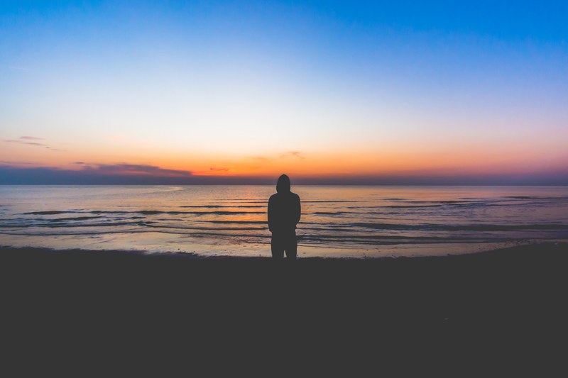 silhouette of a person standing on the beach at the edge of rippling water watching the sunset, riccione beachfront sunset 4k