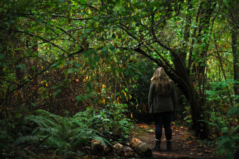 a woman on a dirt path through a dense green thicket, woman exploring a forest 4k