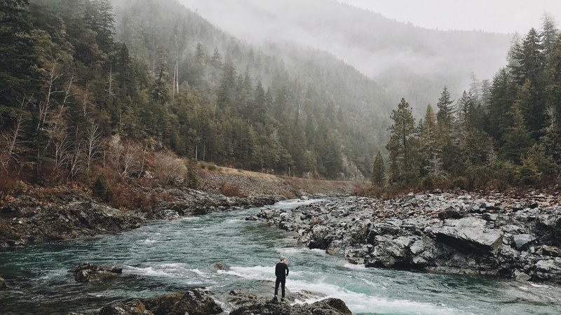 a man standing on jagged rocks in a fast flowing river in the wilderness, man in a bubbling river 4k