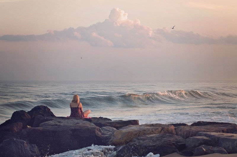 woman sitting on the rock looking at the ocean waves at sunset, woman sitting on the rock 4k