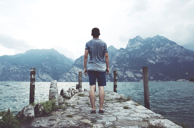 a man standing on a stone jetty over a choppy lake with mountains on the opposite shore, stone jetty on a cloudy day 4k