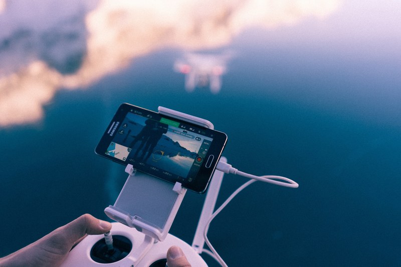 a hand controlling a drone and watching its video through an iphone, drone flying 4k