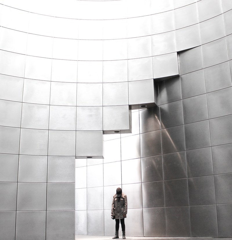 person in a coat stands near a shiny silver wall in a grid pattern, all the way up 4k