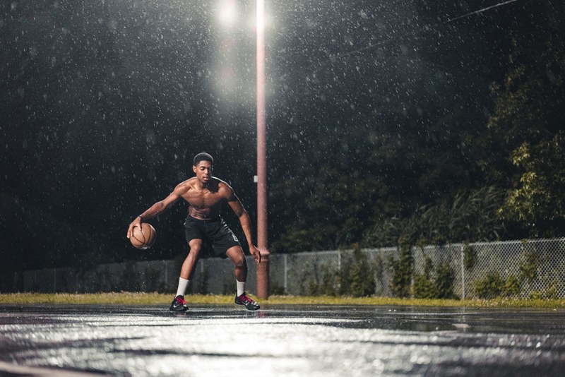 athletic man playing basketball alone on a court in the rain, relentless_ 4k