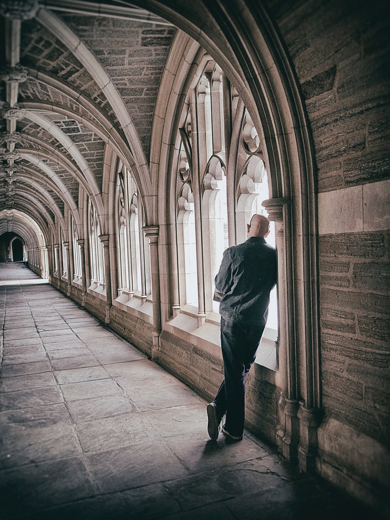 man leaning against wall in gothic medieval hallway architecture near windows with light coming through, medieval windows and man 4k