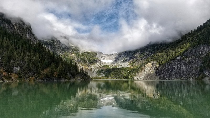 a lake surrounded by mountains on a cloudy day, clouds over a lake 4k