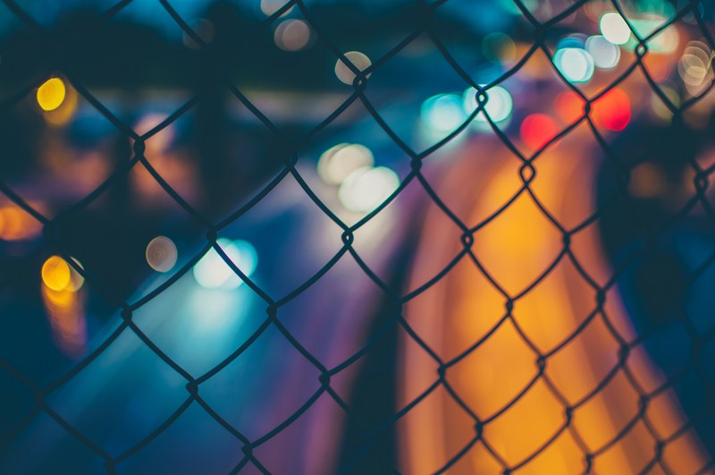 a blurry shot from behind a fence of traffic trails on the highway in the background, traffic trail light shot 4k