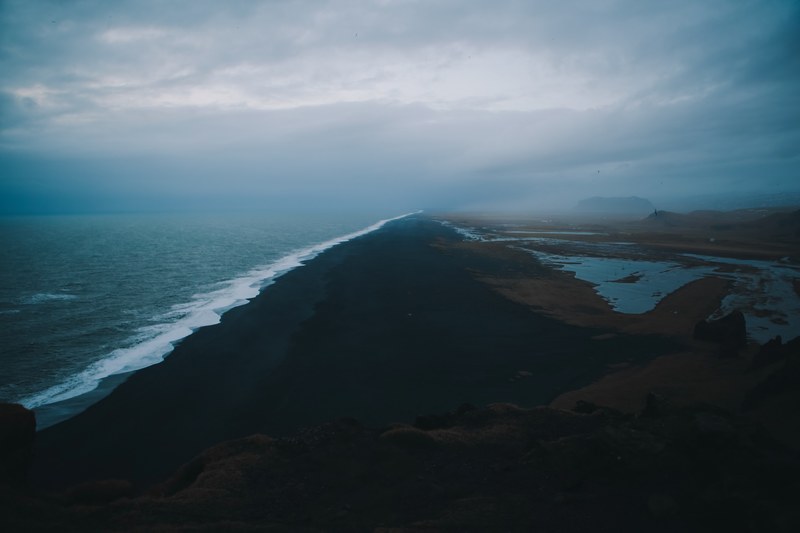 drone view of empty black sand beach shoreline on a cloudy day, the black sand beach 4k