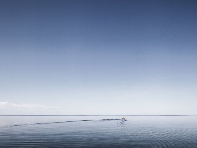 a small boat leaves ripples on the smooth surface of water stretching to the horizon, sailing towards the horizon 4k