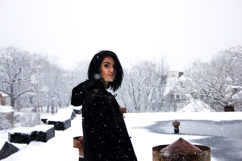 a dark haired woman in a black coat on a snowy roof of looking back, on the snowy rooftop 4k
