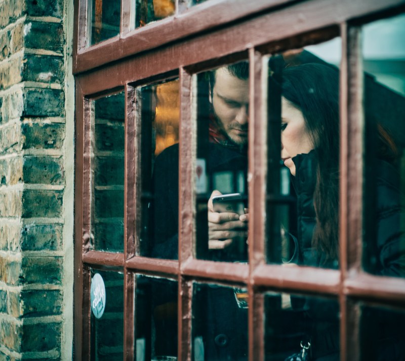 couple standing indoors by a window in camden lock looking at an iphone, should we call for help 4k