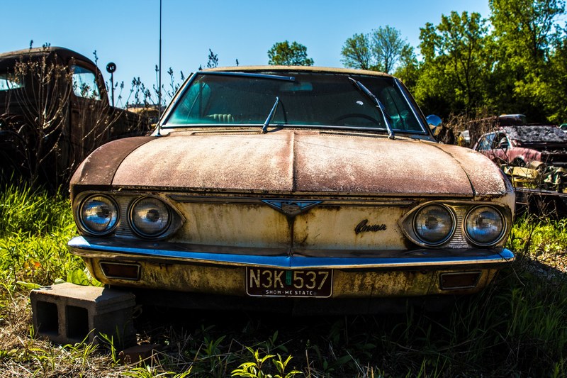 front of a rusty abandoned fender with a license plate and headlights in a car junkyard, rusty fender car junkyard 4k