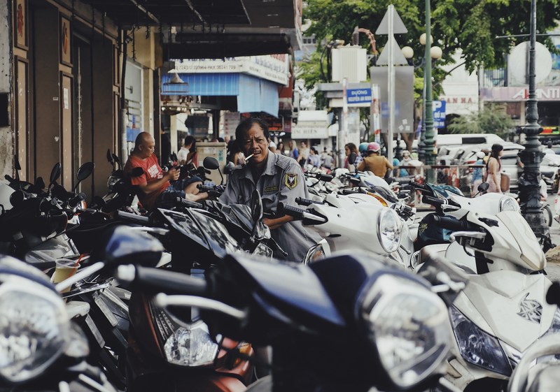 a man smokes a cigarette while standing among an array of motor scooters in the city, man smoking with scooters 4k