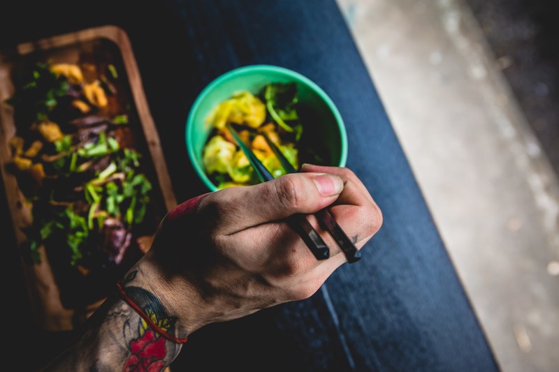 hand with a tattoo eating salad and pasta with chopsticks, eating with chopsticks 4k