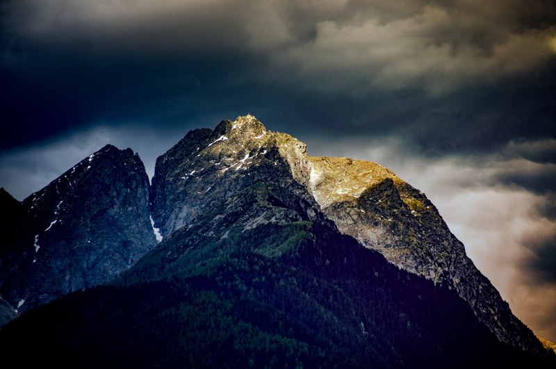 a dramatic view of a mountain illuminated by rays of light under thick gray clouds, dark mountains 4k
