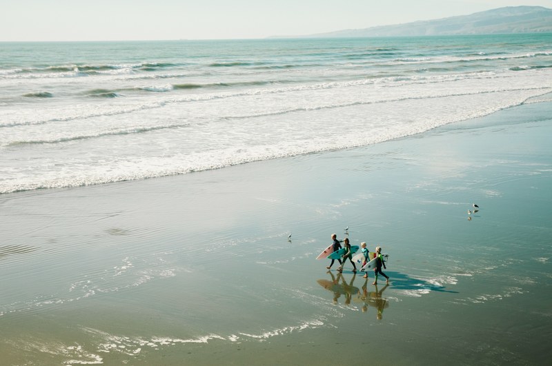four surfers walk along the beach with their brightly colored surfboards, _surfing friends heading for the sea 4k