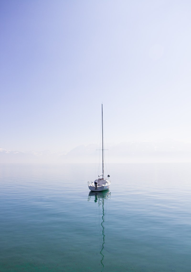 lone sailboat sitting on a calm blue lake on a sunny day in lausanne, serene sailboating 4k