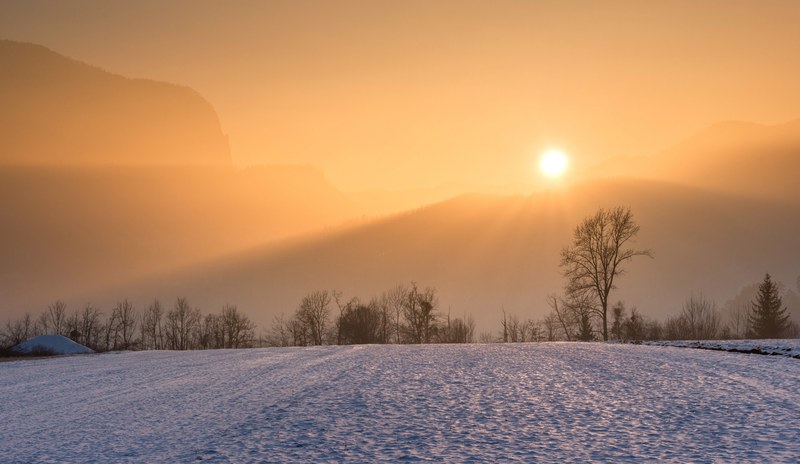 golden rays of the sunset hit a barren snowy valley with mountains and trees in the distance, golden sunset 4k