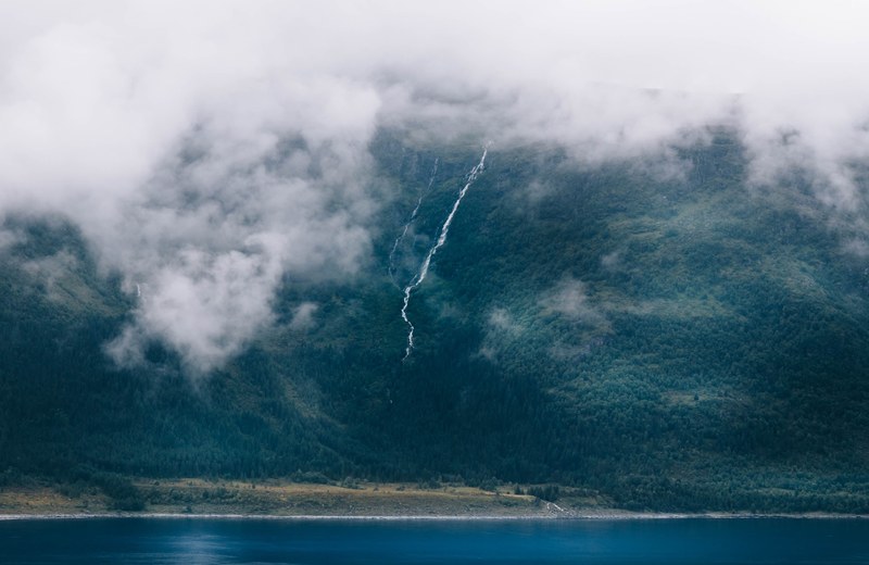 mist rolling down a wooded slope near a lake in lesund, mist creeping towards a lake 4k