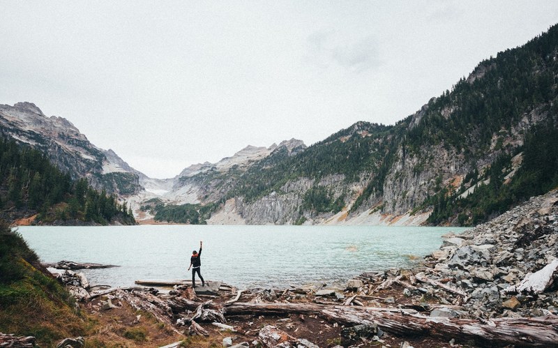 a woman raising her hand in a triumphant gesture on the edge of a mountain lake, celebrating on the lake 4k