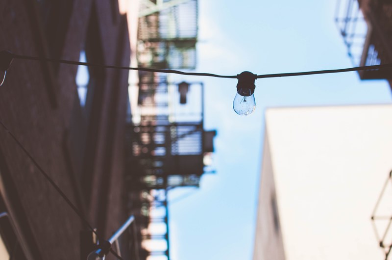 a lightbulb hangs on a cable running between two buildings against a blue sky, off duty lightbulb 4k