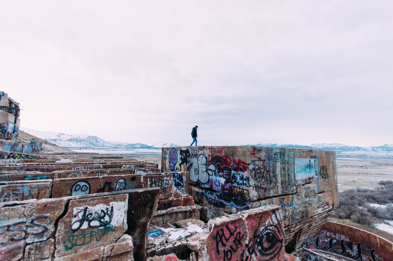 person walking on concrete structure covered in graffiti in isolated region, graffiti covered architecture 4k