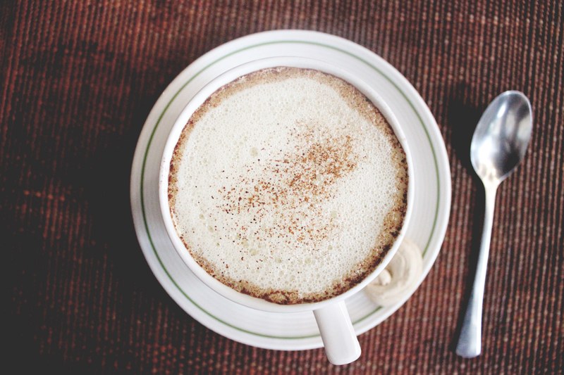 a frothy cup of coffee with cinnamon sprinkled on top of it in a white mug, frothy coffee 4k