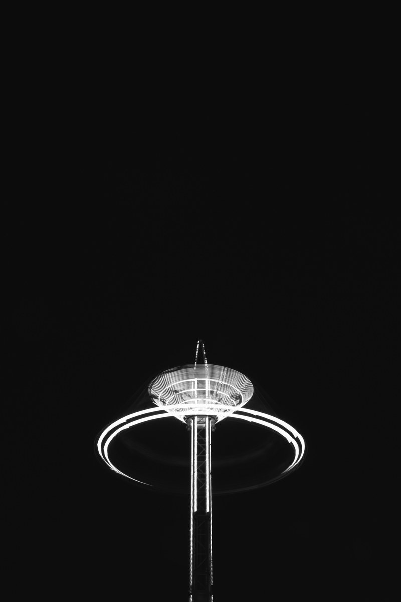 a black ground with an illuminated fairground ride lit up with a surrounding light trail circle, illuminated wolverhampton fairground ride 4k