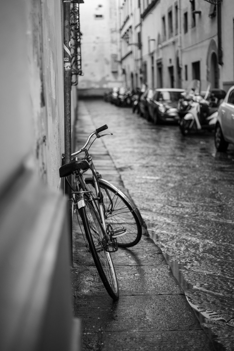 black and white shot of bike leaning against wall in street with cars and heavy rain, bike on rainy street 4k