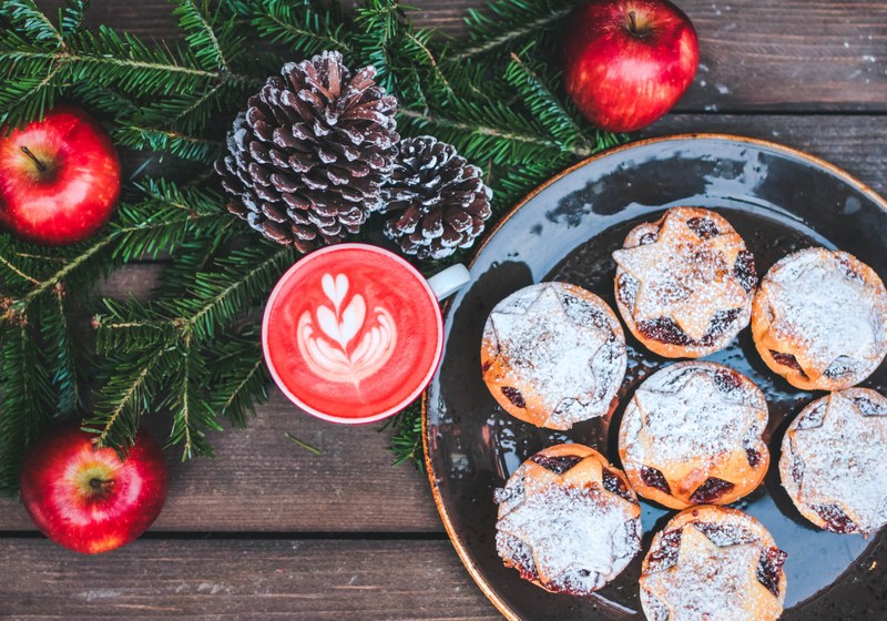 a festive set up of apples pine leaves acorns and mince pies in london, red velvet cappuccino 4k