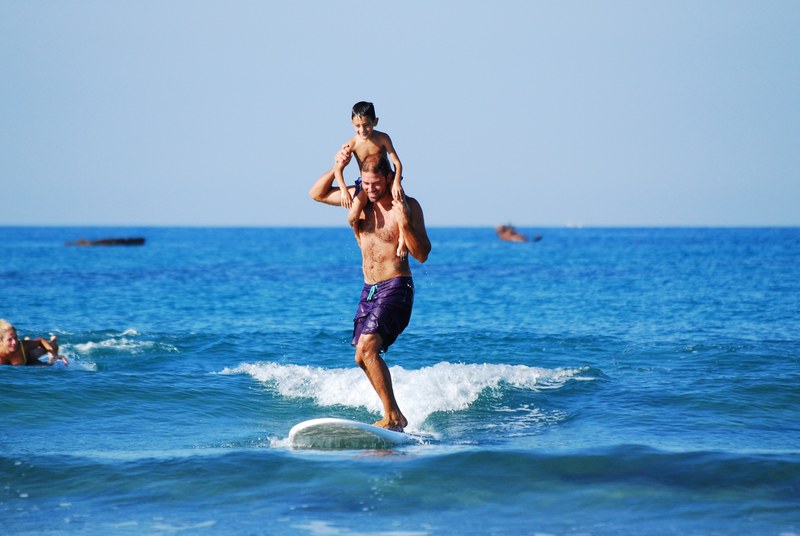 boy on his fathers shoulders who is surfing on a board, smiling with a big smile 4k