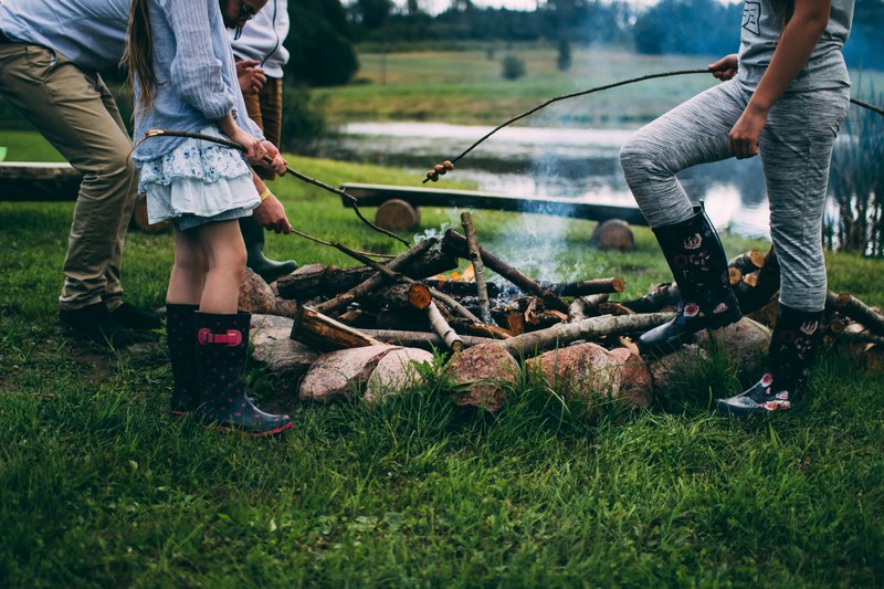 a family standing around a campfire wearing wellies roasting marshmallows in rgi, rgi campfire 4k
