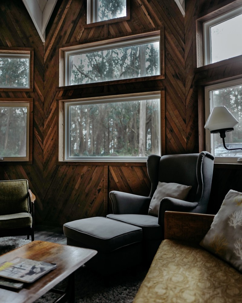 black ottoman leans against rustic styled windows nestled in a forest, retreat at the oyster suite 4k