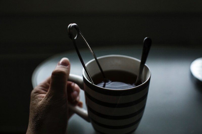 striped tea mug with tea and a spoon inside being held by the left hand, dark teatime 4k