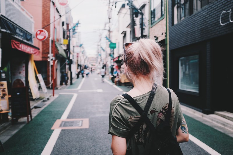 a woman in a ponytail and t shirt walks down a street by shops in shimo kitazawa station, zen capital 4k