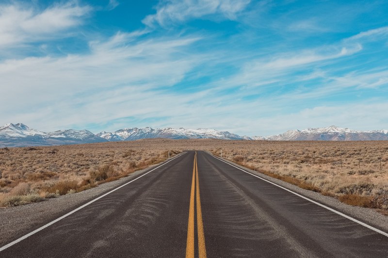 a long empty asphalt road through dry plains with snowy mountains on the horizon, long road into the mountains 4k