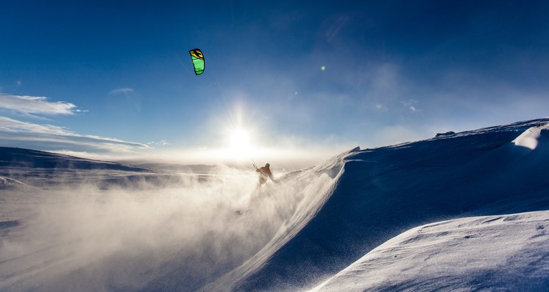 a silhouette of kiteboarder kicking up snow on a mountain, mountain kiteboarder 4k