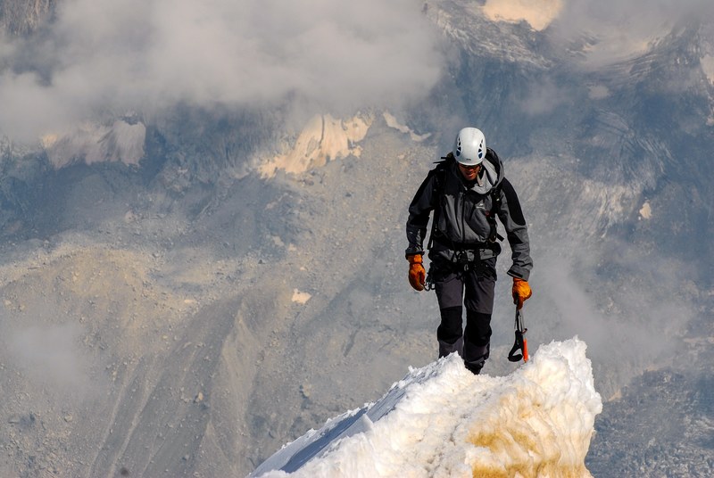 one climber making it to the top surrounded by clouds and snowy mountains, mountain climber in mountains 4k