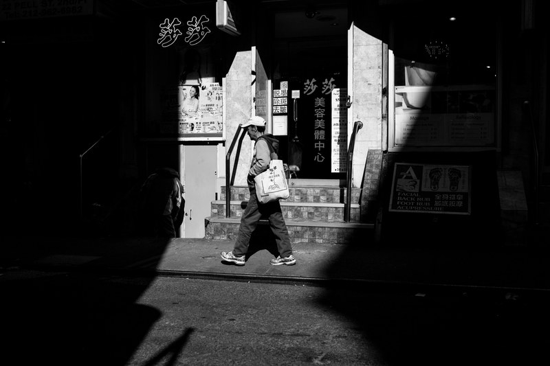 black and white shot of person walking on sidewalk past shop in chinatown with shadow, chinatown shop and person 4k