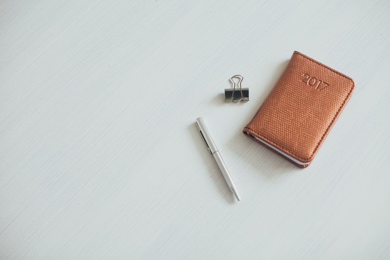 a small notebook with a leather cover next to a pen and a bulldog clip, leather notebook 4k