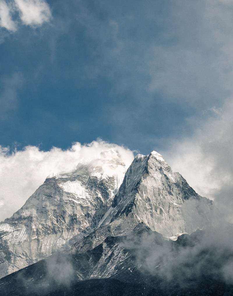 two mountain peaks cut through clouds towards a blue sky, years past 4k