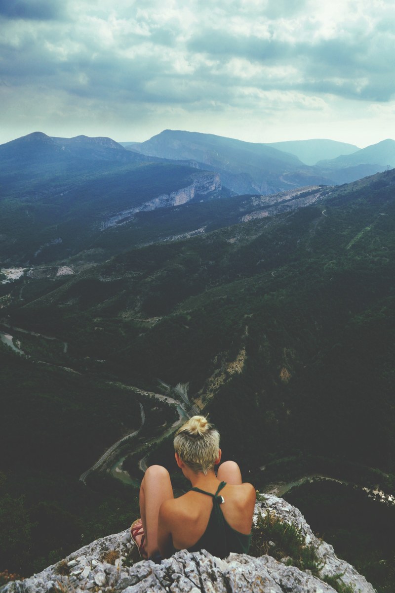 a young woman sitting on a rocky ledge overlooking a fertile mountain valley, taking in the beauty of the mountain valley 4k