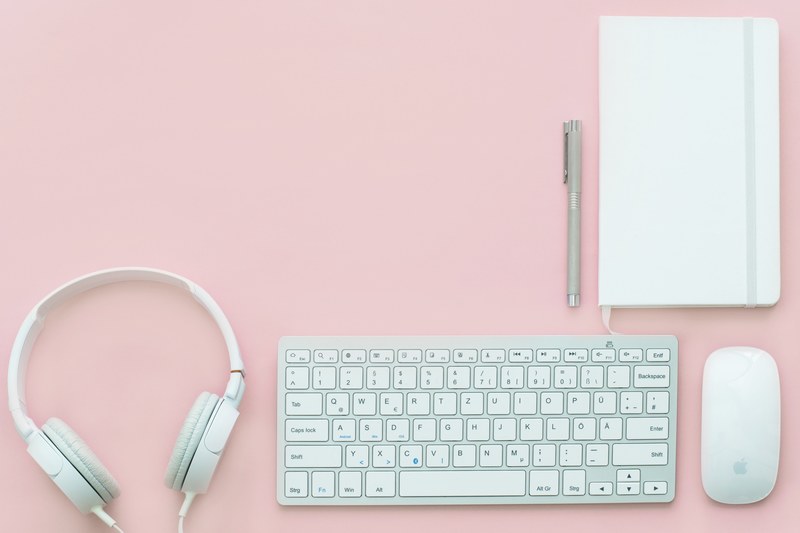 a flatlay with a white notebook keyboard headphones and mouse on a pink surface, white gear on pink flatlay 4k