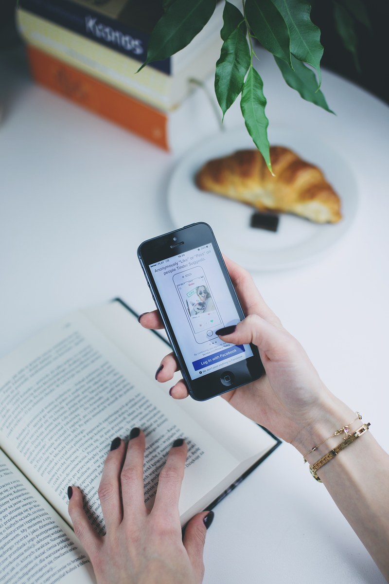 a person using tinder on an iphone while reading a book at a desk with a croissant, tinder book and croissant 4k